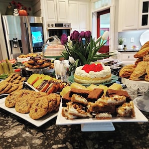 A kitchen counter with various baked goods, a cake with a strawberry on top, and a decorative cow figurine.