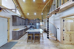 A modern kitchen with a central island, wooden cabinets, and a spiral staircase. - Charming Cabin with Private River Access & Firepit in Ashton, Idaho (Ashton)