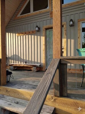 A wooden deck with a railing, a bench, and a table with chairs. - Charming Cabin with Private River Access & Firepit in Ashton, Idaho (Ashton)