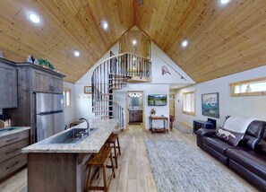 A spacious kitchen with a central island, a dining area with a sofa, and a living room with a fireplace. - Charming Cabin with Private River Access & Firepit in Ashton, Idaho (Ashton)