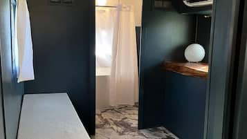 Un espacio interior estrecho con un banco, un estante pequeño con un objeto esférico y una zona de ducha con cortinas.