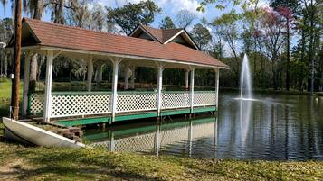 Ein überdachter Pavillon mit Dach, einer Anlegestelle und einem Springbrunnen in einer Parkanlage.