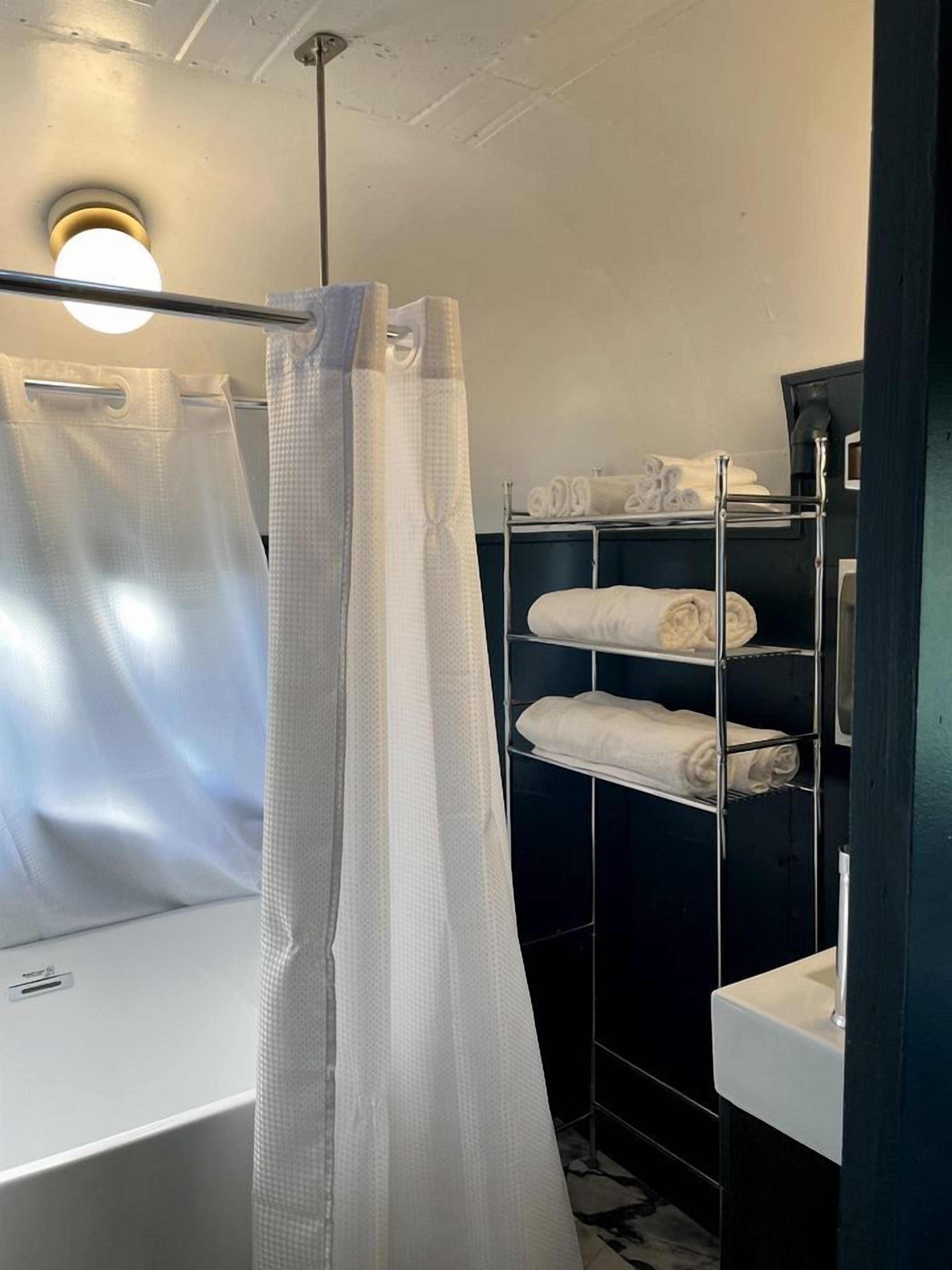 Ein Badezimmer mit Duschvorhang, einem Metallhandtuchhalter mit Handtüchern und einem weißen Waschbecken.
