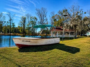 A boat with the number 'MJ 201 BC' on a grassy area near a body of water, with a gazebo and a house in the background. - Vintage Shasta Camper with Peaceful Fire Pit Retreat in Midway, Georgia (Midway)
