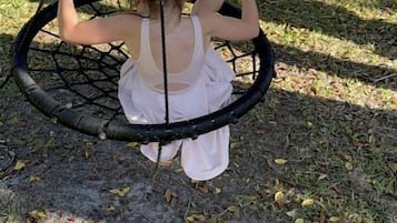 A person on a swing in a park with grass and trees in the background.