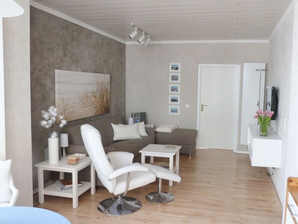 Ein modernes Wohnzimmer mit einem weißen Sofa, einem weißen Sessel, einem Couchtisch und einem Beistelltisch mit einer Vase und einer Lampe.