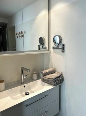A modern bathroom with a white vanity, a sink, a mirror, and a towel stack. - Holiday Apartment With 1 Bedroom (Norderney)