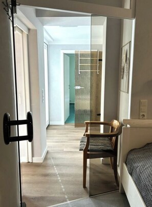 A narrow hallway with a wooden floor, a chair, a bed, and a door with a black handle. - Holiday Apartment With 1 Bedroom (Norderney)