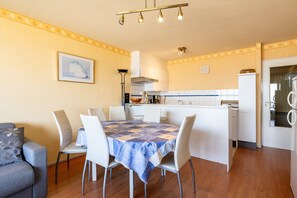 A compact kitchen with a dining area, featuring a table with chairs, a refrigerator, and a clock on the wall. - Seaside Apartment in Blankenberge With Sea Views (Blankenberge)