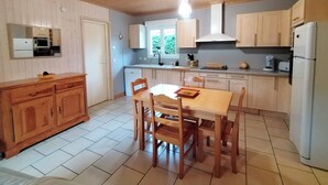 Cocina compacta con armarios de madera, una mesa de comedor con sillas, horno empotrado y refrigerador.