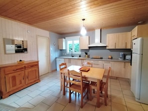 Cozinha compacta com armários de madeira, mesa de jantar com cadeiras, forno embutido e geladeira.