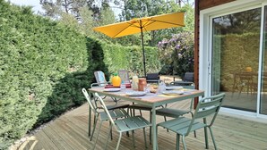 Un área de comedor al aire libre con una mesa dispuesta para cuatro personas, rodeada de sillas y cubierta por un paraguas amarillo.