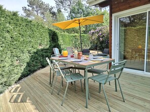 Uma área de refeiç ões ao ar livre com uma mesa posta para quatro pessoas, rodeada de cadeiras, sob um guarda-sol amarelo.