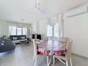 A living room with a sofa, a TV, a fireplace, and a dining table with chairs. - REQUESENS 116 Empuriabrava – INTERimmo (Empuriabrava)