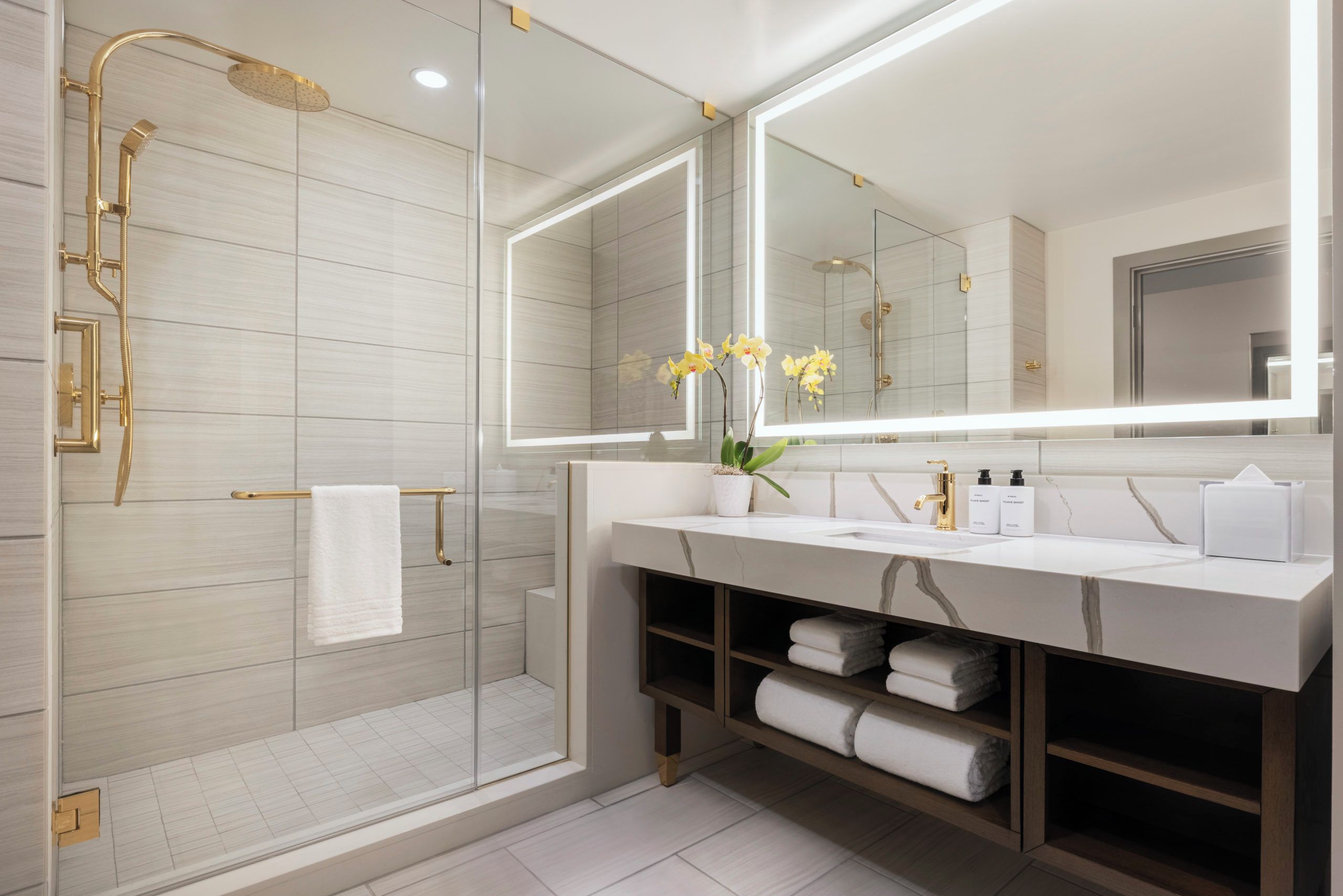 A modern bathroom with a glass shower enclosure, a vanity with a large mirror, and a potted orchid.