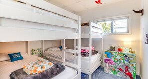 Ein Schlafraum mit Etagenbett, einem Fenster, einem Schreibtisch mit farbigem Fischdesign und einem Kissen mit Strandmotiv.