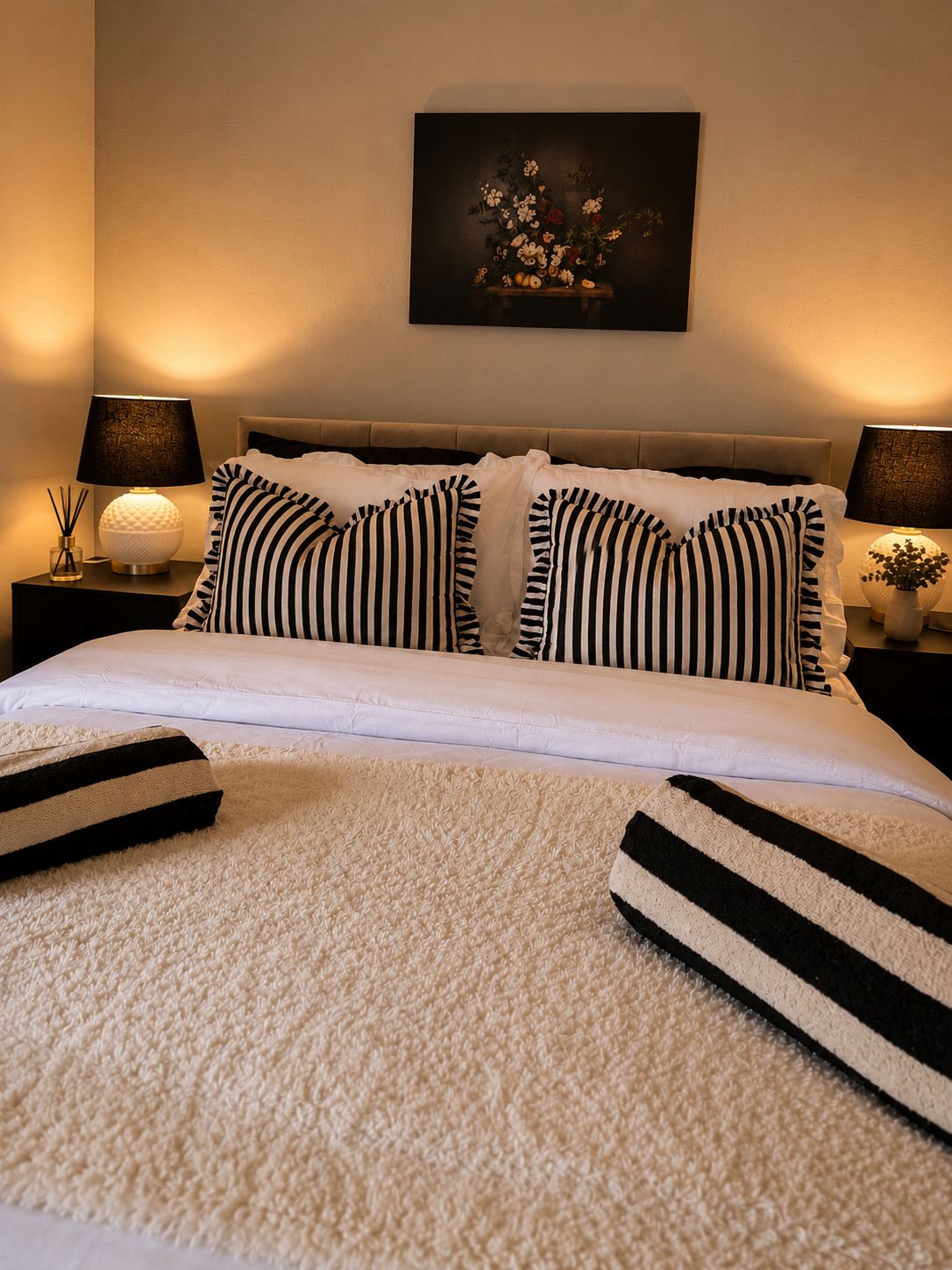 A neatly made bed with striped pillows, a white duvet, and a fluffy white rug.