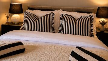 A neatly made bed with striped pillows, a white duvet, and a fluffy white rug.