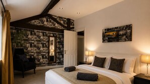 Quarto com uma cama grande, mesa de cabeceira, cadeira, parede com pintura de paisagem urbana e porta que dá para outro cômodo.