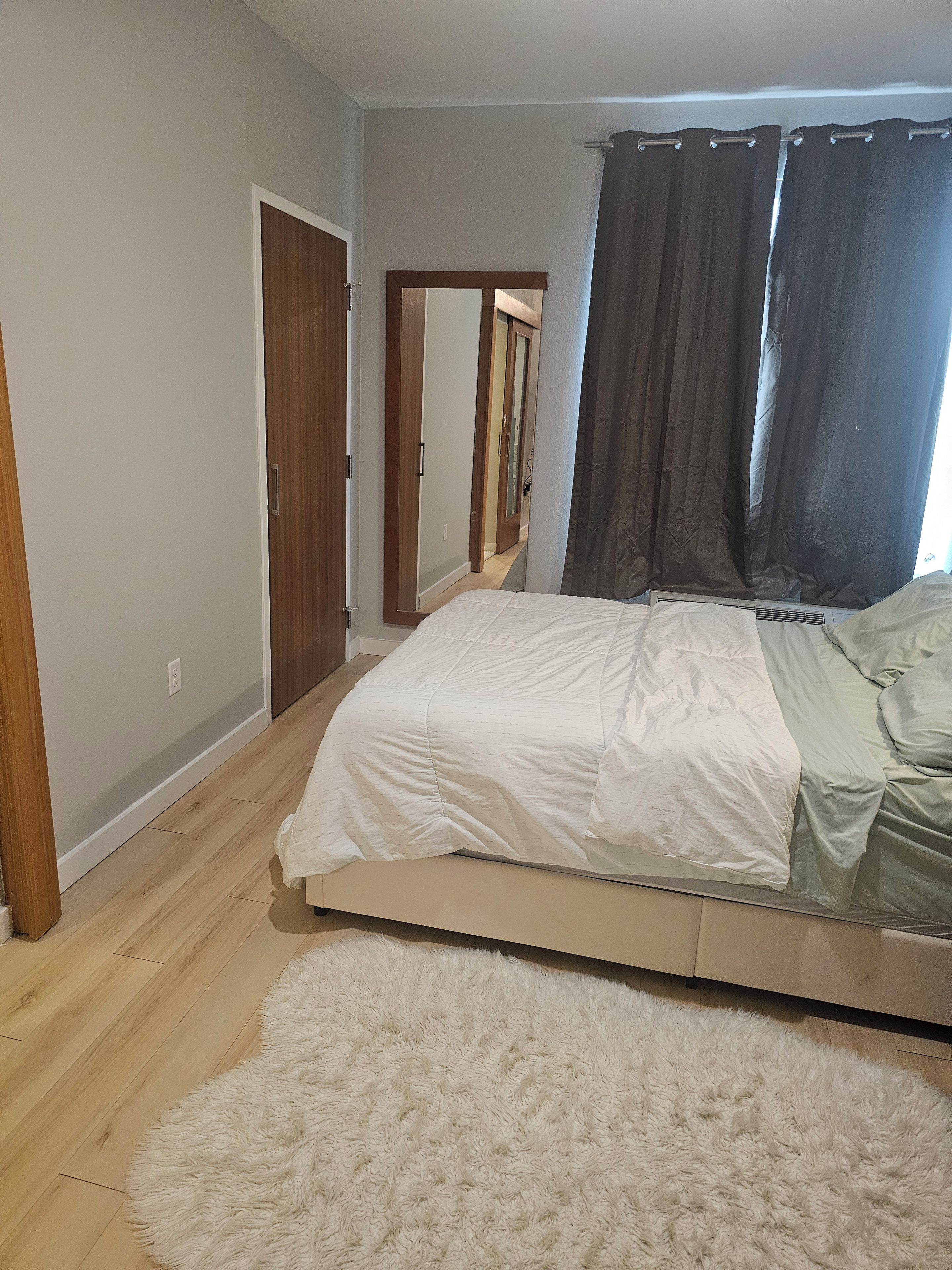 A bedroom with a bed, a fluffy rug, a wooden door, and a window with curtains.