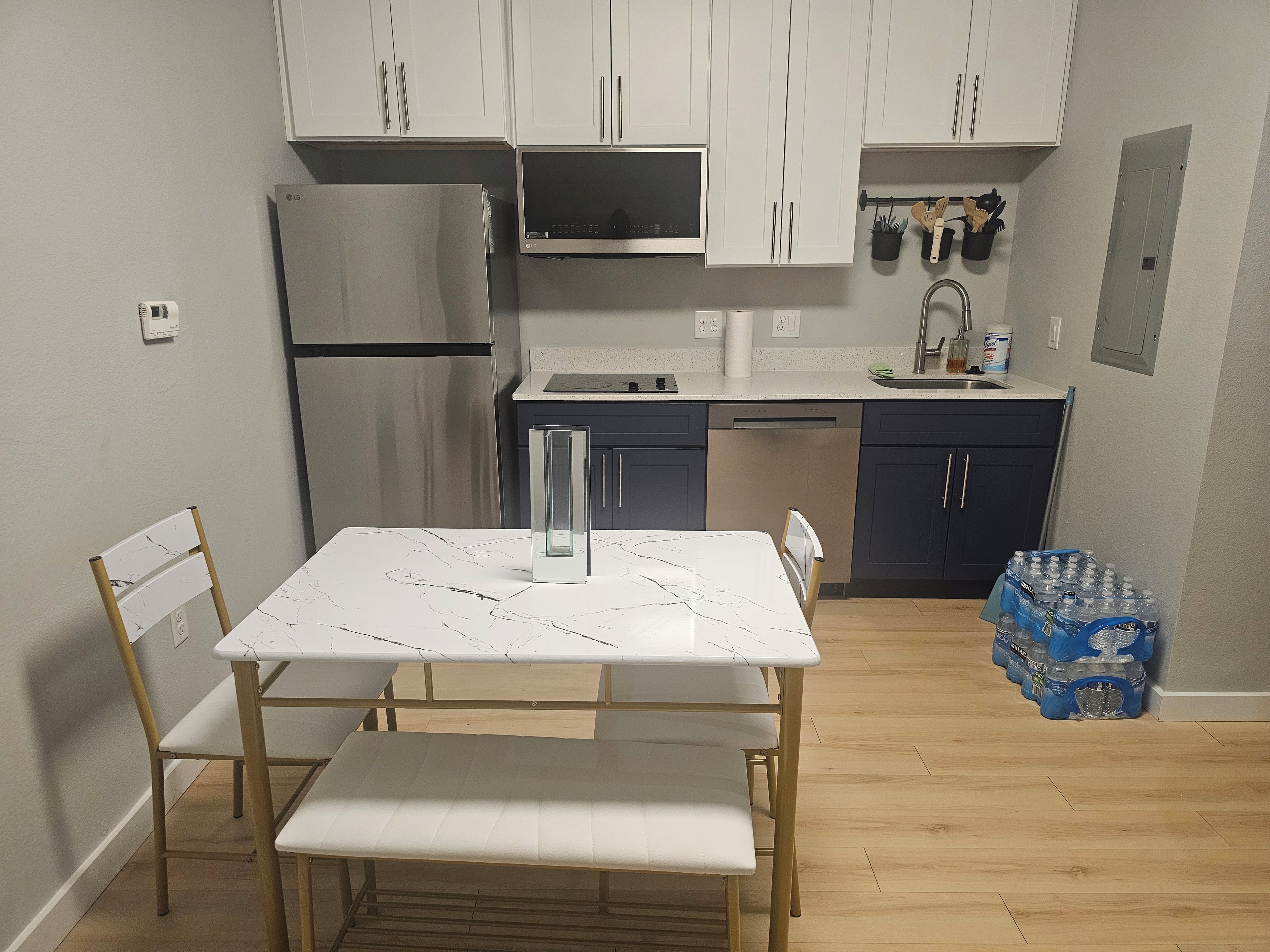 A compact kitchen with white cabinets, a stainless steel refrigerator, a dishwasher, and a dining area with a marble table and chairs.
