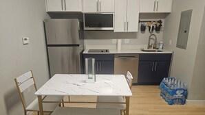 A compact kitchen with white cabinets, a stainless steel refrigerator, a dishwasher, and a dining area with a marble table and chairs. - Cozy 1-bedroom studio apartment in perfect Houston with fitness room and AC, (Houston)