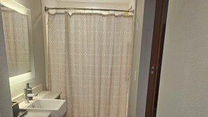 A bathroom with a sink, mirror, shower curtain, and two mats on the floor. - Cozy 1-bedroom studio apartment in perfect Houston with fitness room and AC, (Houston)