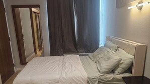 A bedroom with a bed, a bedside table, a fluffy rug, and a window with curtains. - Cozy 1-bedroom studio apartment in perfect Houston with fitness room and AC, (Houston)