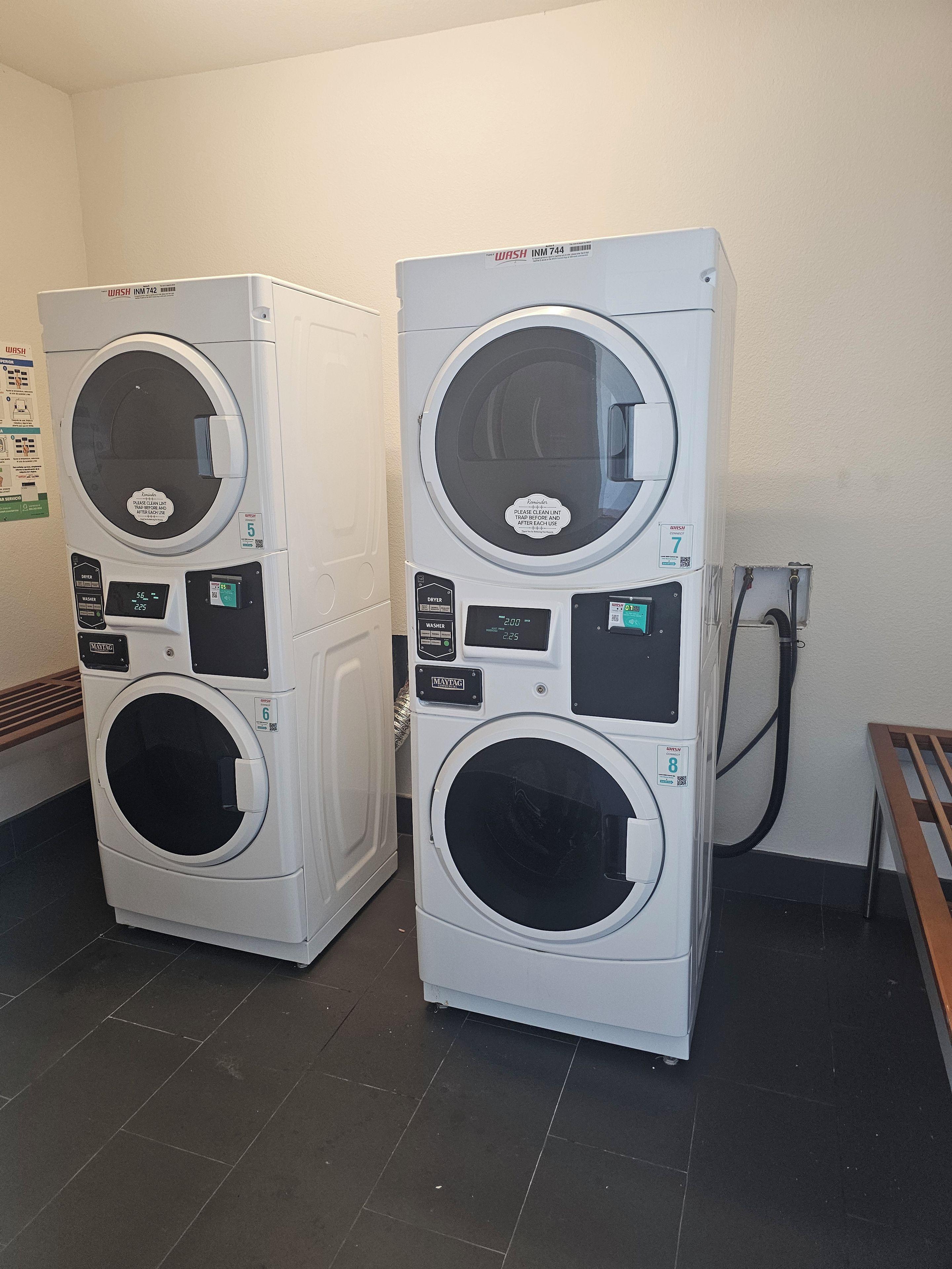Two front-loading washing machines in a room with a tiled floor and a wooden bench.