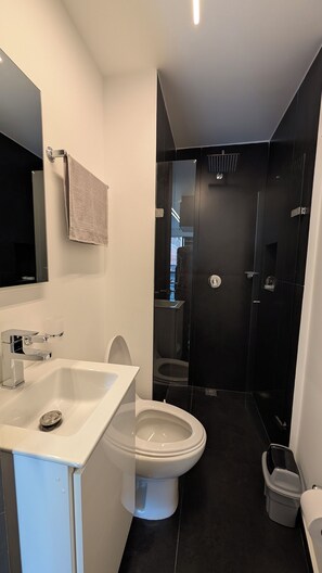 Et moderne badeværelse med en hvid vask, toilet og en brusekabine med glas.