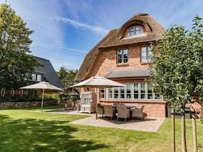 Ein Backsteinhaus mit Strohdach, eine Terrasse mit Gartenmöbeln und einem gepflegten Rasen.