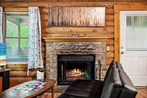 Ein gemütliches Wohnzimmer mit Kamin aus Stein, Holzwänden, einer schwarzen Ledersofa und einem Tisch mit Zeitschriften.