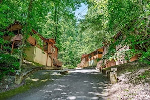 A forested area with wooden cabins, a paved path, and a small stream. - Rustic Cabin with Hot Tub & Cozy Stone Fireplace Retreat in Sevierville, Tennessee (Sevierville)