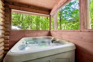 A hot tub in a wooden cabin with a view of a forest. - Rustic Cabin with Hot Tub & Cozy Stone Fireplace Retreat in Sevierville, Tennessee (Sevierville)