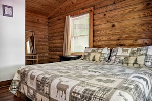 Ein Schlafzimmer in einer Blockhütte mit einem Bett, einem Fenster mit Jalousien und einem Holzkopfende.