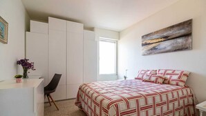 Ein Schlafzimmer mit einem Bett, einem Schreibtisch, einem Stuhl, einem Kleiderschrank und einem Fenster.