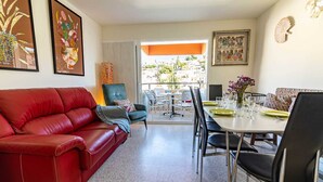 Ein Wohnzimmer mit einem roten Ledersofa, einem grünen Sessel und einem Essbereich mit Tisch für vier Personen.