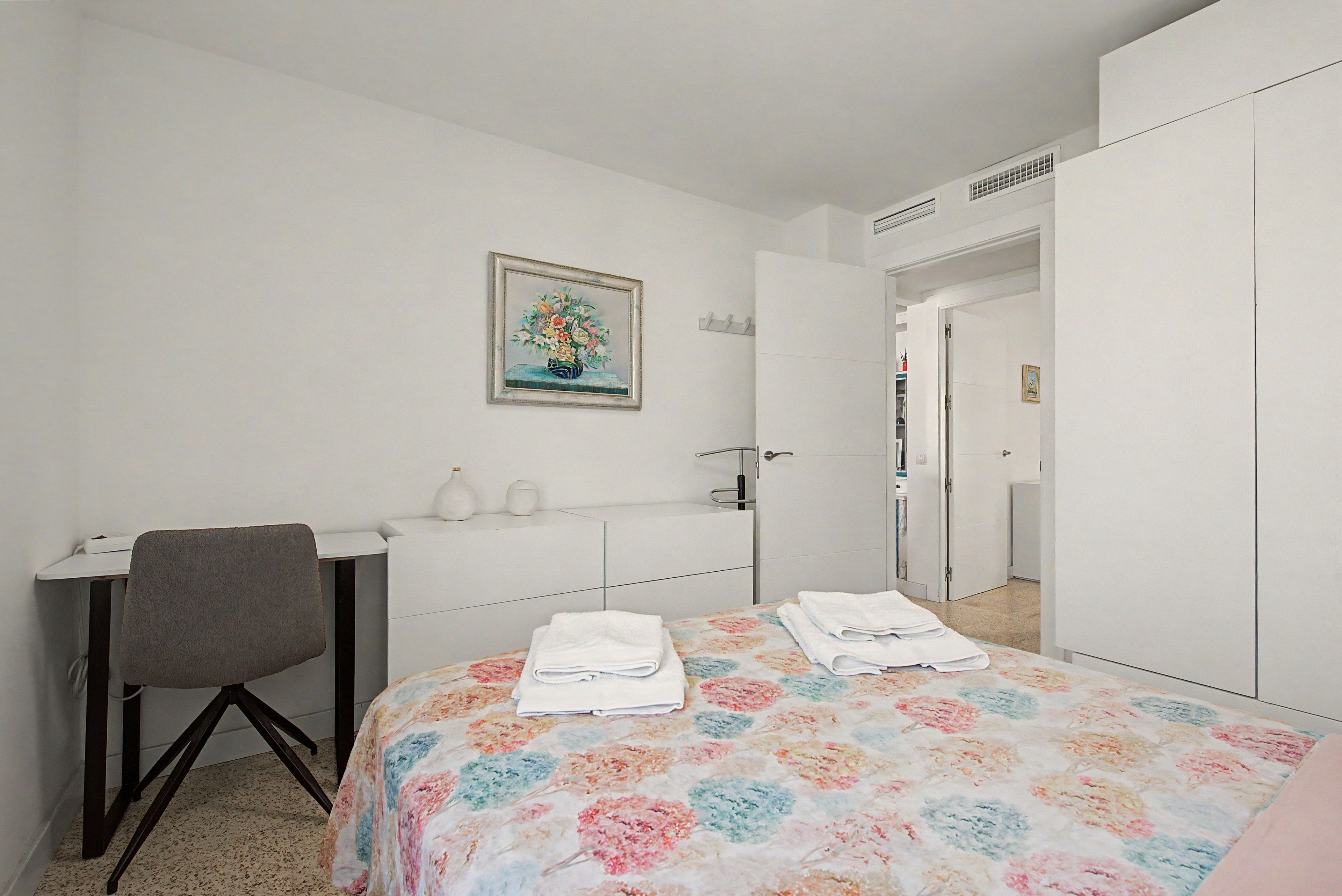 Un dormitorio con cama, escritorio, silla, armario y una puerta que da a otra habitación.