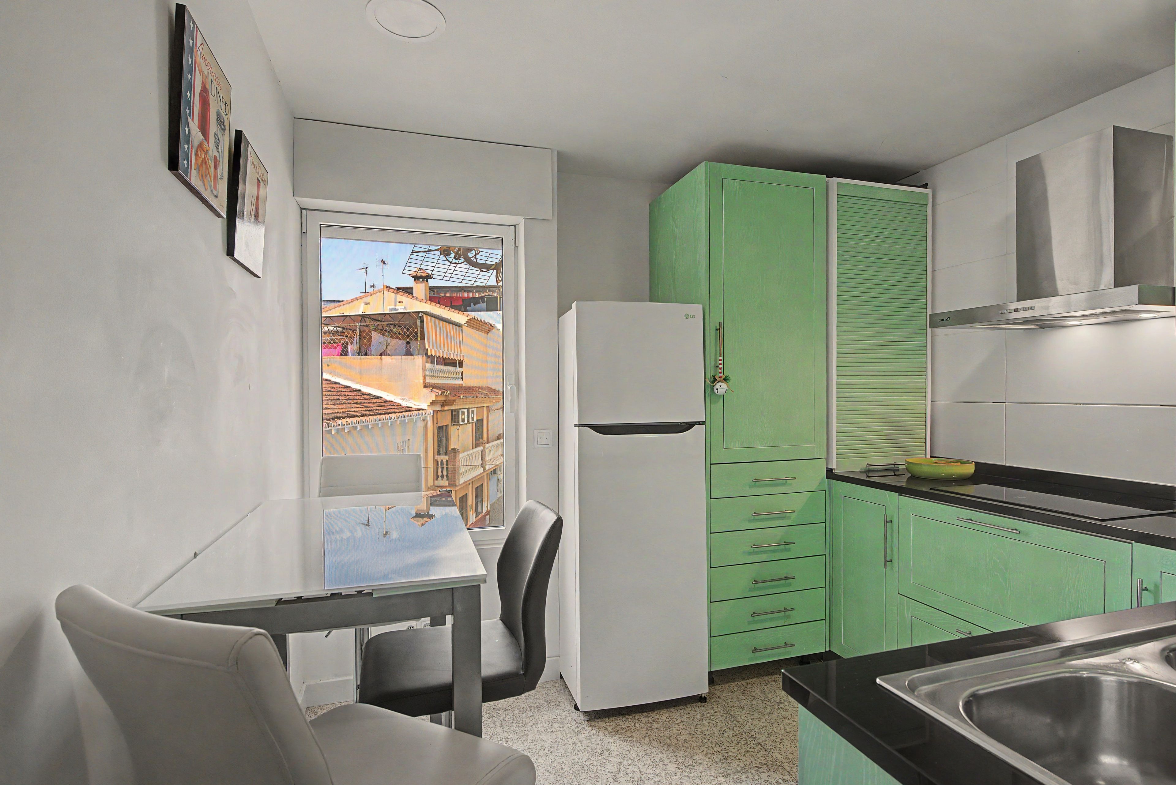 Una cocina compacta con refrigerador, una mesa de comedor con sillas y gabinetes verdes.