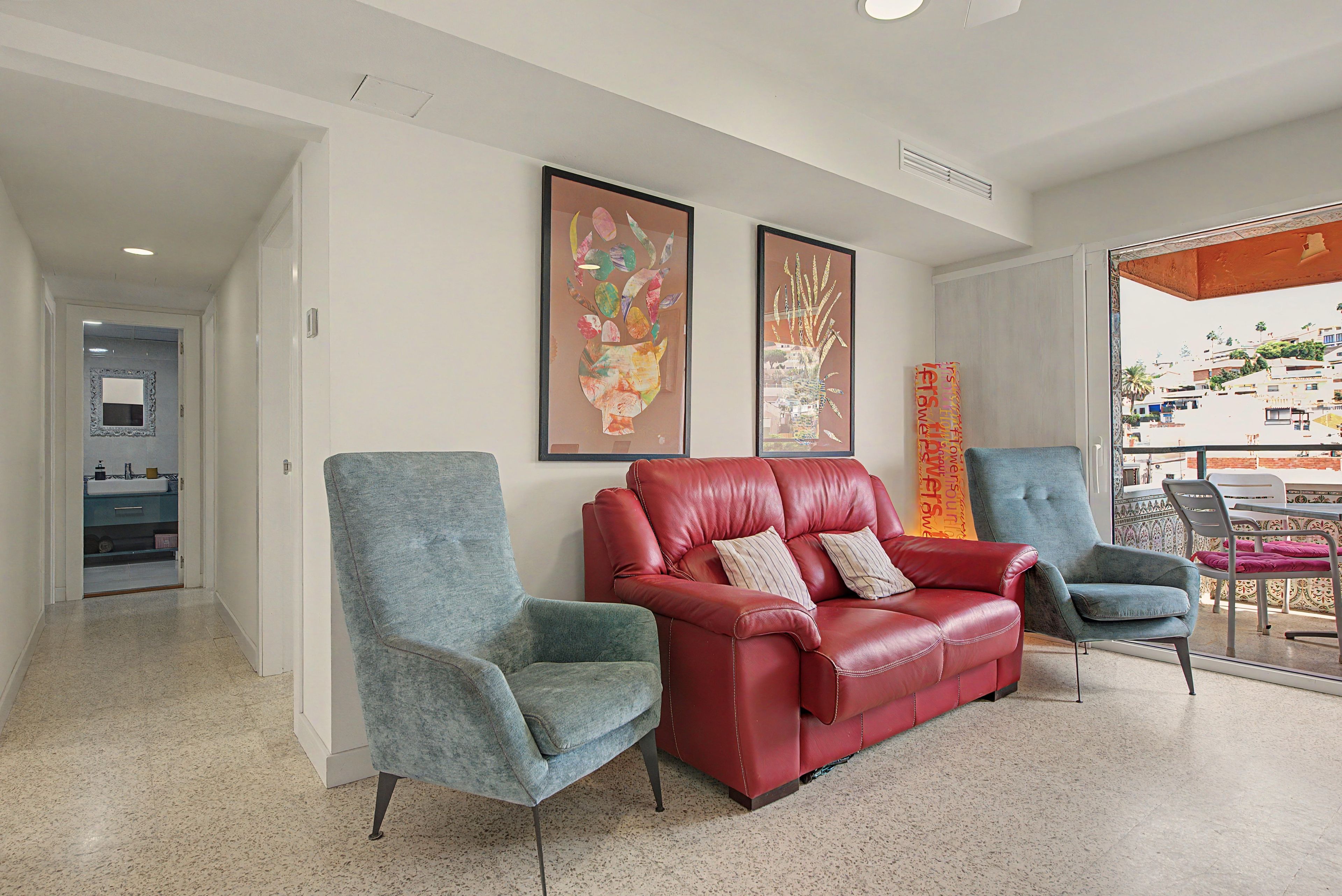 Una sala de estar moderna con un sofá de cuero rojo, dos sillones y un ventanal con vistas a la ciudad.
