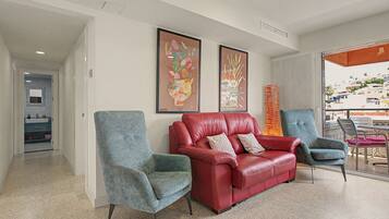 Una sala de estar moderna con un sofá de cuero rojo, dos sillones y un ventanal con vistas a la ciudad.