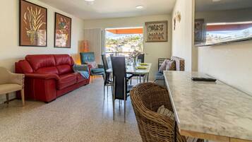 Una sala de estar con un sofá rojo, una mesa de comedor con sillas y una cocina visible a través de una puerta abierta.