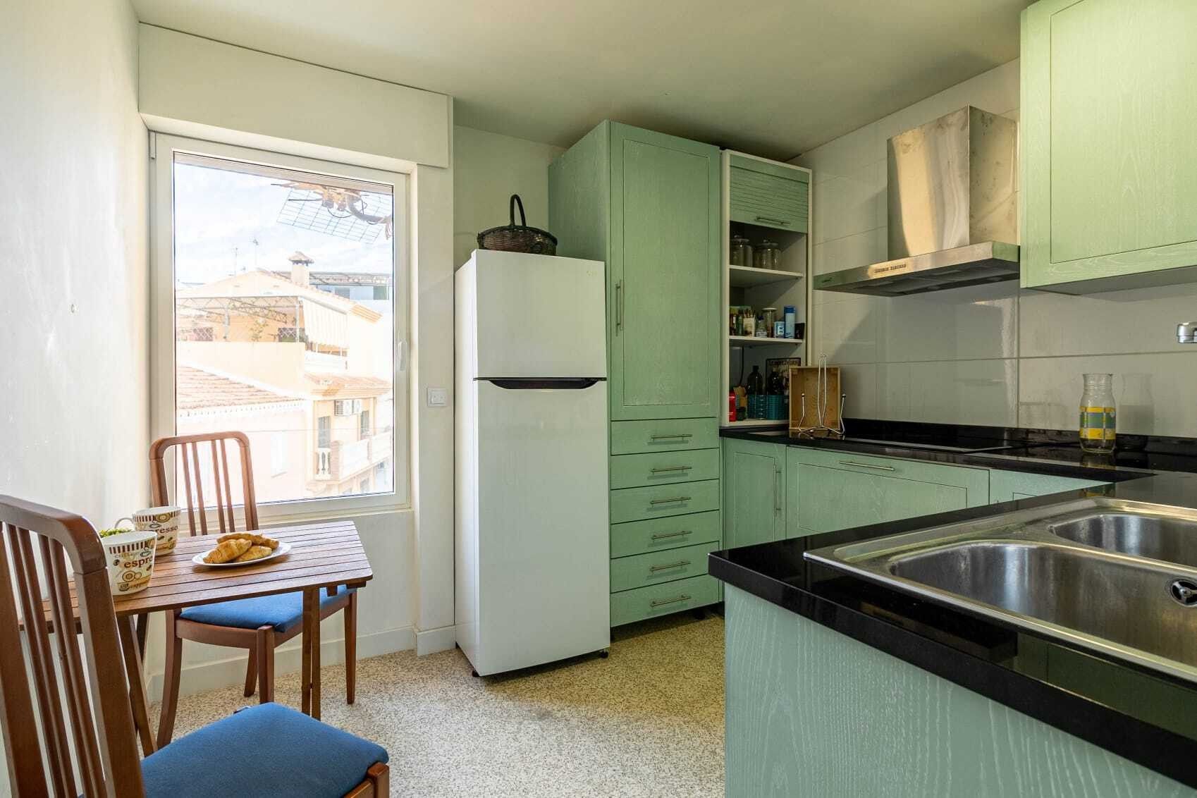 Eine kompakte Küche mit Kühlschrank, Schränken und einer Essecke mit Tisch und Stühlen.