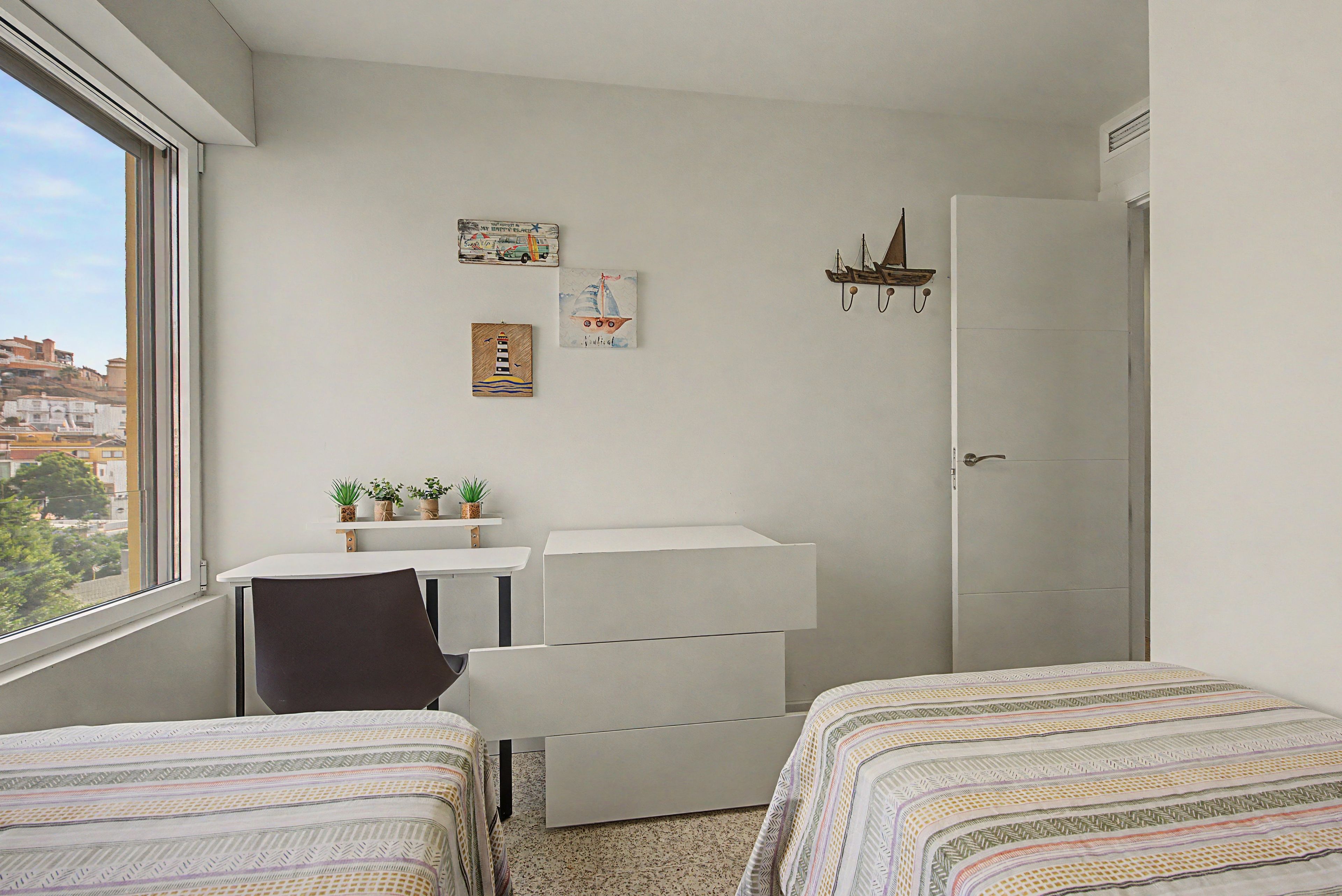 Una habitación pequeña y ordenada con dos camas, un escritorio y una ventana.