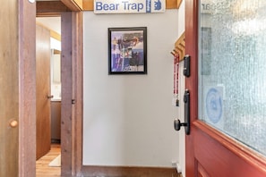 A hallway with a framed photograph on the wall, a door with a glass panel, and a sign above the door. - Cozy Cabin Condo | Near Northstar Village (Truckee)