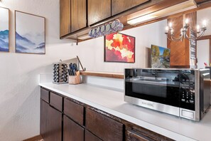 A kitchen with a stainless steel microwave, wooden cabinets, and various kitchen utensils. - Cozy Cabin Condo | Near Northstar Village (Truckee)