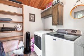 A laundry area with a washing machine, dryer, and shelves with folded clothes. - Cozy Cabin Condo | Near Northstar Village (Truckee)