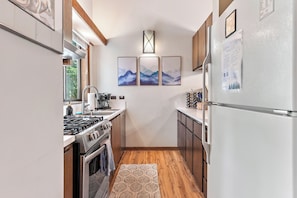 A compact kitchen with a gas stove, oven, and a refrigerator. There are wooden cabinets and a patterned rug on the floor. - Cozy Cabin Condo | Near Northstar Village (Truckee)