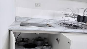 Une cuisine équipée d’un plan de travail, d’un égouttoir et de divers appareils de cuisine, notamment un cuiseur à riz et des casseroles.