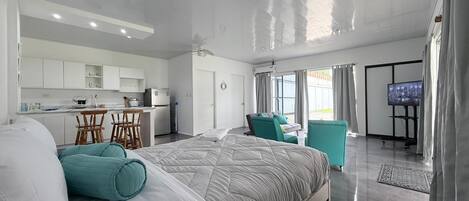 Quarto de hotel moderno com uma cama grande, cozinha compacta, área de refeições e televisão.